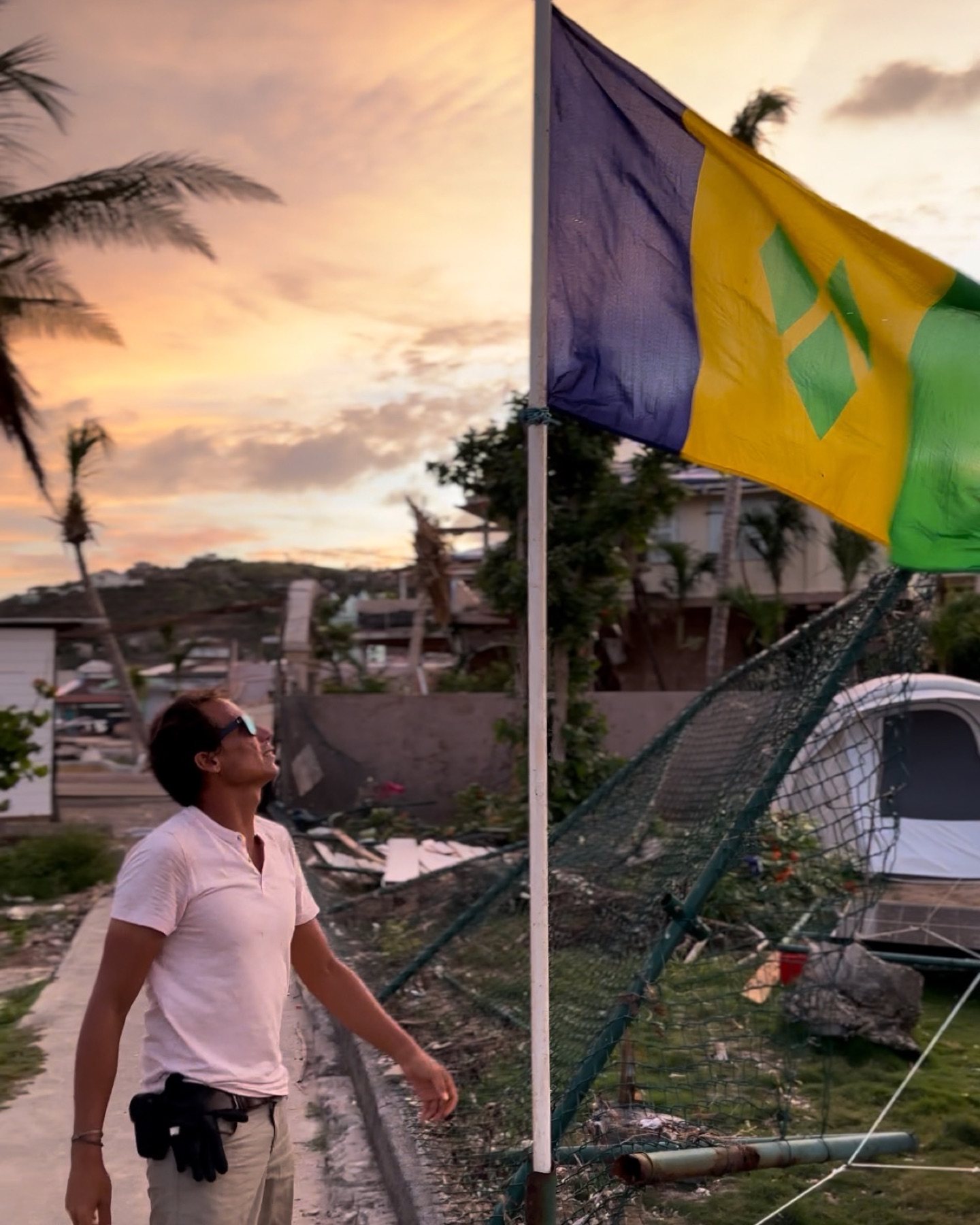 Jeremie Tronet looking up at the Saint Vincent and the Grenadines flag after Hurricane Beryl